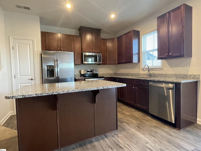 kitchen with stainless steel appliances, a center island, light stone countertops, light hardwood / wood-style flooring, and sink