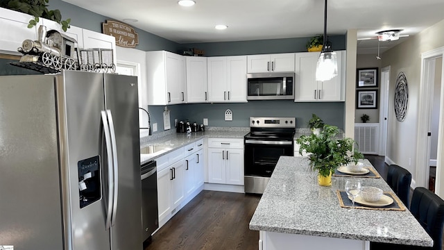 kitchen with light stone countertops, pendant lighting, appliances with stainless steel finishes, dark wood-type flooring, and white cabinetry