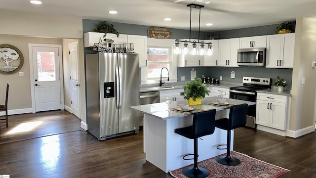 kitchen featuring decorative light fixtures, a kitchen island, light stone countertops, stainless steel appliances, and white cabinets