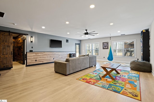 living room with ceiling fan, a barn door, and light wood-type flooring