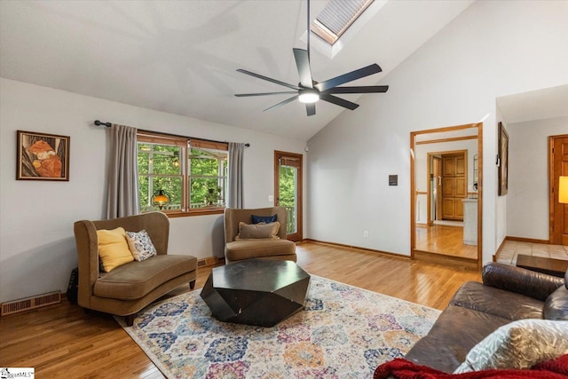 living room with high vaulted ceiling, a skylight, ceiling fan, and light hardwood / wood-style floors