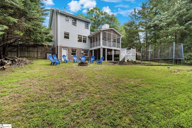 back of house with an outdoor fire pit, a trampoline, a yard, and a sunroom