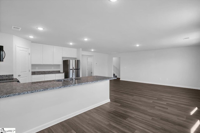 kitchen with dark hardwood / wood-style flooring, dark stone countertops, stainless steel refrigerator, white cabinets, and sink