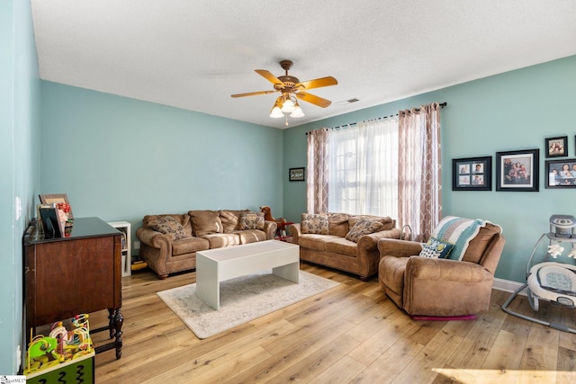 living room featuring ceiling fan, a textured ceiling, and light hardwood / wood-style flooring