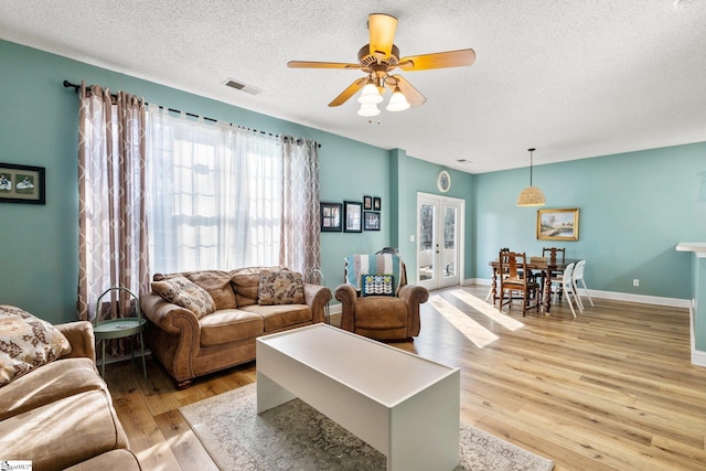 living room featuring ceiling fan, a textured ceiling, light hardwood / wood-style flooring, and french doors