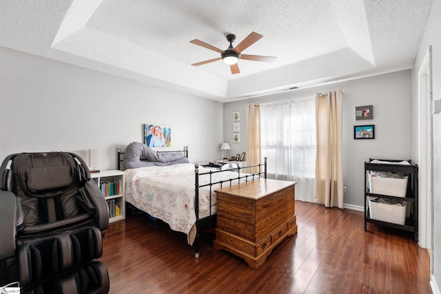 bedroom with a textured ceiling, ceiling fan, dark wood-type flooring, and a tray ceiling