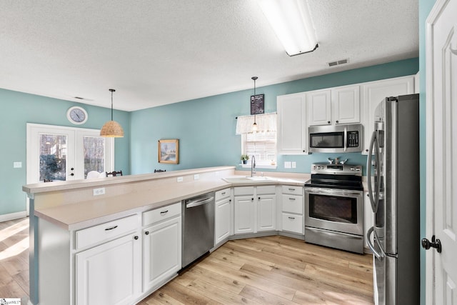 kitchen featuring appliances with stainless steel finishes, french doors, pendant lighting, white cabinets, and sink