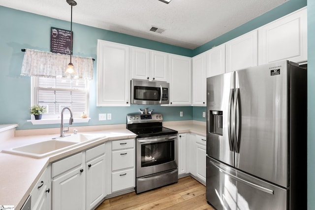 kitchen with appliances with stainless steel finishes, pendant lighting, white cabinetry, and sink