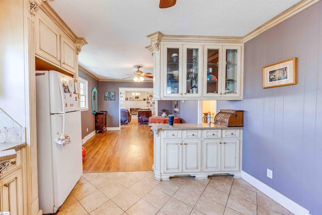 kitchen with white refrigerator, ornamental molding, cream cabinetry, and light tile patterned flooring