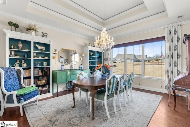 dining space with a raised ceiling, crown molding, an inviting chandelier, and hardwood / wood-style flooring