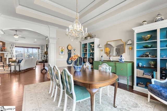 dining space with hardwood / wood-style flooring, a tray ceiling, a fireplace, ornamental molding, and ceiling fan with notable chandelier