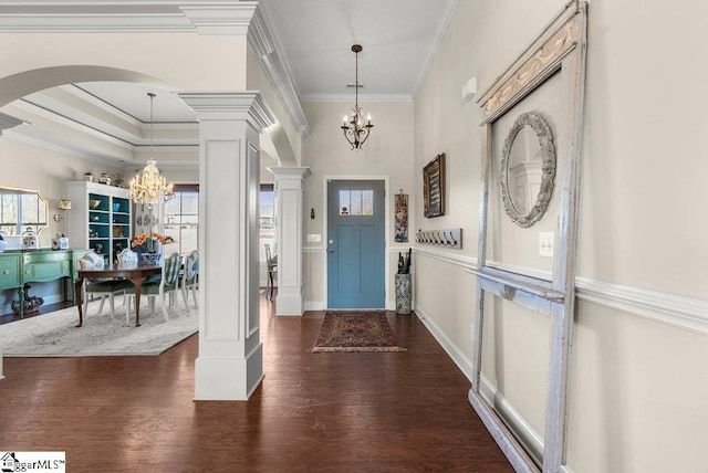 foyer entrance featuring decorative columns, dark hardwood / wood-style flooring, ornamental molding, and an inviting chandelier