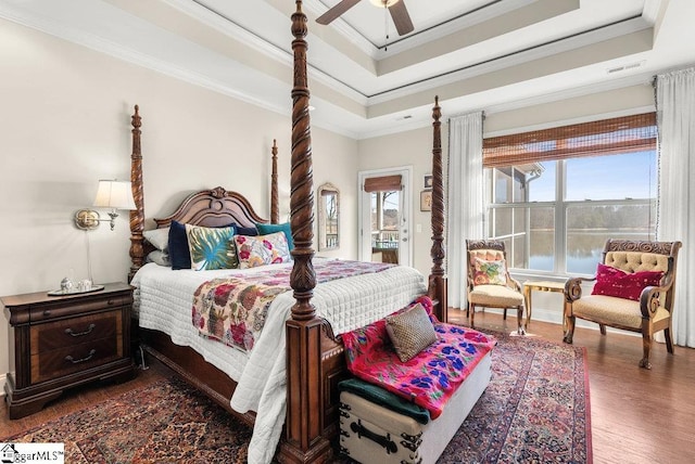 bedroom with ceiling fan, a raised ceiling, wood-type flooring, crown molding, and a water view