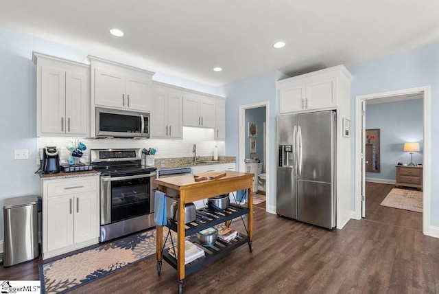 kitchen featuring backsplash, dark wood-type flooring, appliances with stainless steel finishes, white cabinets, and light stone counters