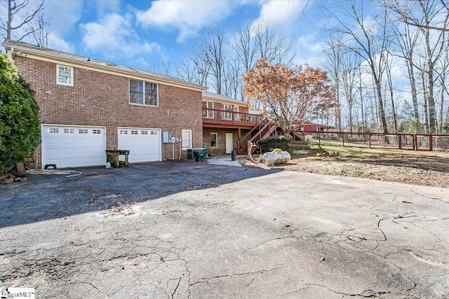 rear view of property with stairs, aphalt driveway, brick siding, and a garage