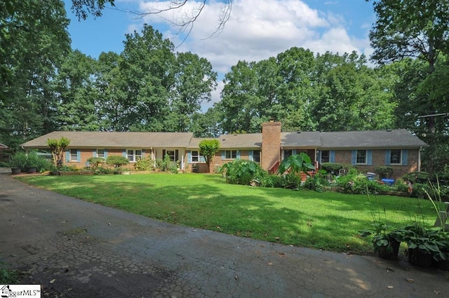 single story home featuring brick siding, a chimney, and a front yard