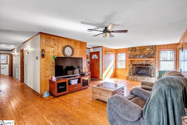 living room featuring ceiling fan, crown molding, plenty of natural light, and a stone fireplace