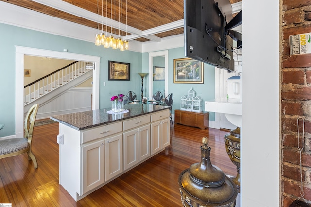 kitchen featuring pendant lighting, white cabinetry, dark stone counters, a center island with sink, and beam ceiling