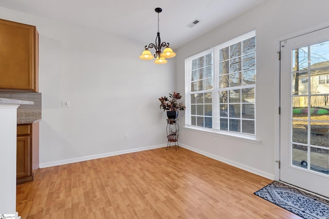 unfurnished dining area featuring an inviting chandelier and light hardwood / wood-style floors