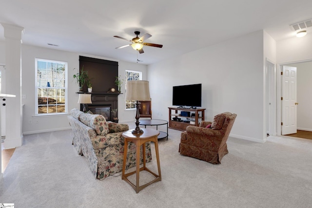 living room featuring decorative columns, a large fireplace, light colored carpet, and ceiling fan