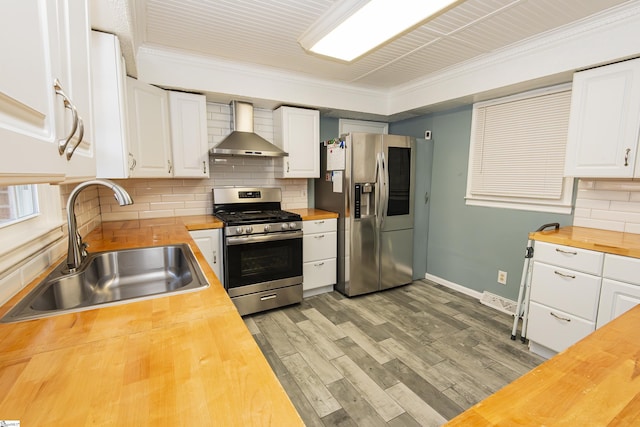 kitchen featuring wall chimney range hood, sink, appliances with stainless steel finishes, white cabinets, and wood counters