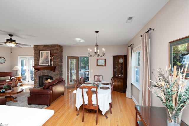 dining space featuring a wealth of natural light, ceiling fan with notable chandelier, a stone fireplace, and light hardwood / wood-style floors