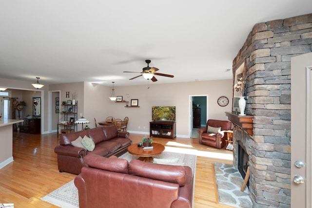 living room featuring ceiling fan, light hardwood / wood-style floors, and a stone fireplace