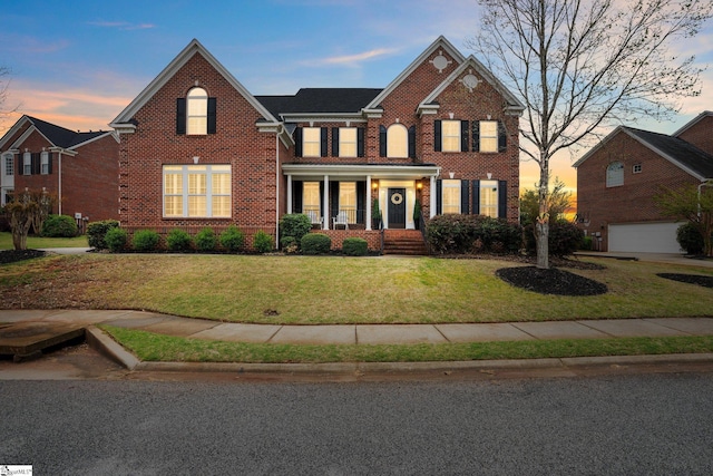 view of front of home with a garage, covered porch, and a lawn