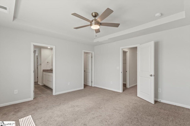 unfurnished bedroom featuring connected bathroom, a tray ceiling, light colored carpet, and ceiling fan