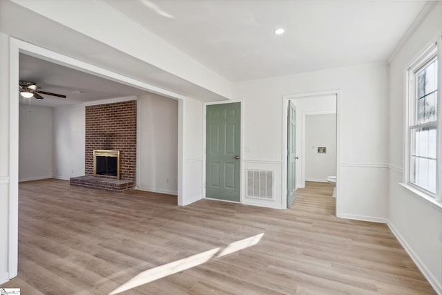 unfurnished living room with a brick fireplace, light hardwood / wood-style floors, ornamental molding, and ceiling fan