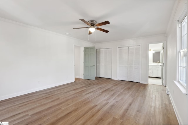 unfurnished bedroom featuring two closets, light wood-type flooring, ceiling fan, ensuite bathroom, and crown molding