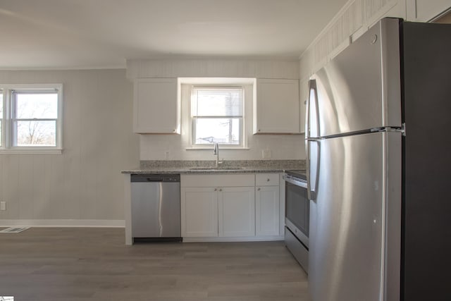 kitchen featuring light stone countertops, white cabinetry, wood-type flooring, stainless steel appliances, and sink