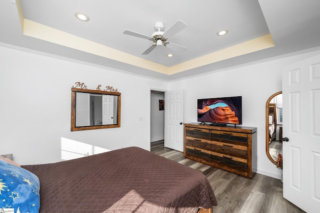 bedroom featuring a raised ceiling, ceiling fan, crown molding, and wood-type flooring