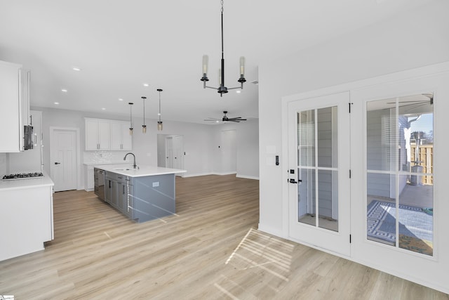 kitchen with ceiling fan with notable chandelier, white cabinets, decorative light fixtures, sink, and a center island with sink