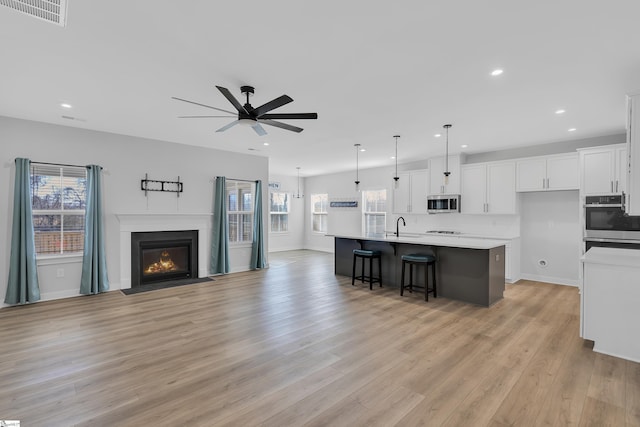 kitchen featuring ceiling fan, light wood-type flooring, hanging light fixtures, a large island with sink, and white cabinets