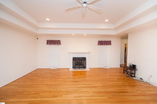 unfurnished living room featuring a tray ceiling, ceiling fan, and light hardwood / wood-style flooring