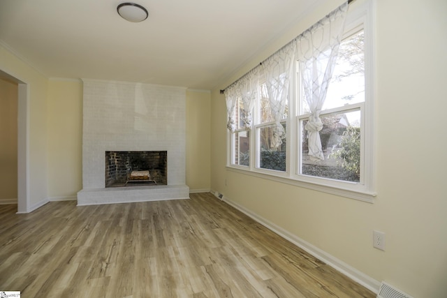 unfurnished living room with a brick fireplace, light hardwood / wood-style floors, and crown molding