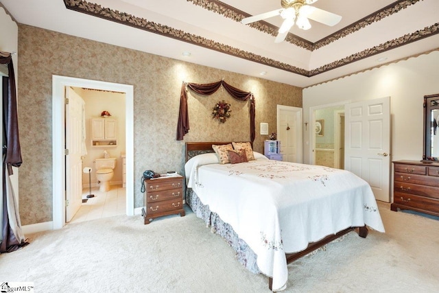 carpeted bedroom with ceiling fan, crown molding, a raised ceiling, and ensuite bath