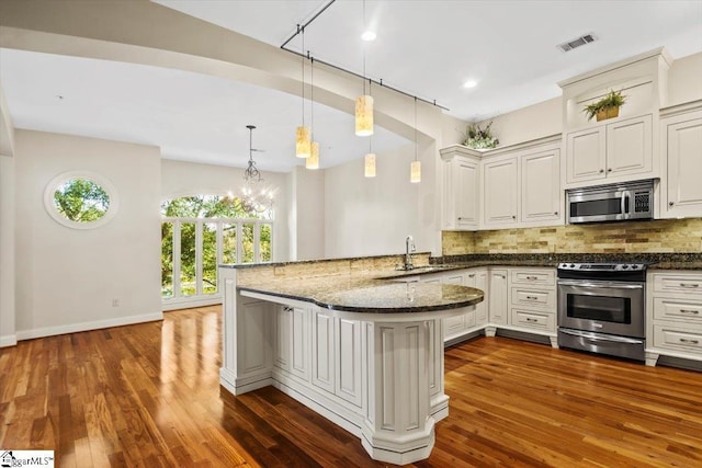 kitchen featuring backsplash, dark stone countertops, kitchen peninsula, sink, and appliances with stainless steel finishes