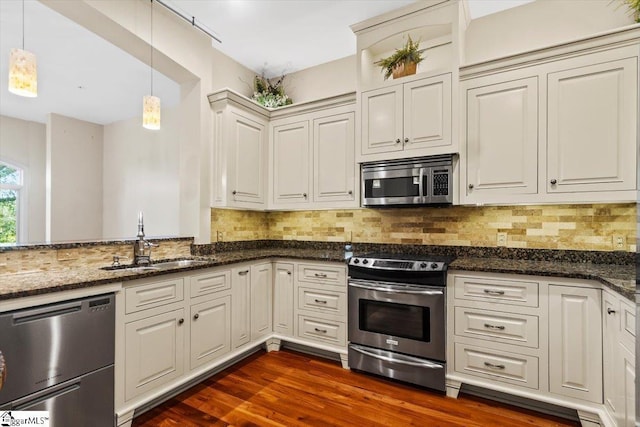 kitchen with hanging light fixtures, appliances with stainless steel finishes, sink, and dark stone counters