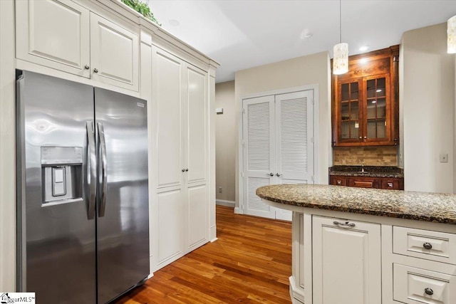 kitchen with decorative light fixtures, stainless steel refrigerator with ice dispenser, decorative backsplash, white cabinetry, and dark stone counters