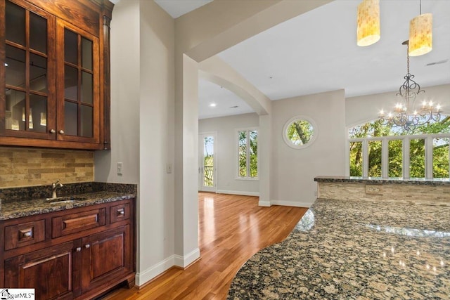 interior space with backsplash, dark stone countertops, sink, an inviting chandelier, and hanging light fixtures