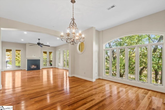 unfurnished living room with light wood-type flooring, a healthy amount of sunlight, ceiling fan with notable chandelier, and french doors