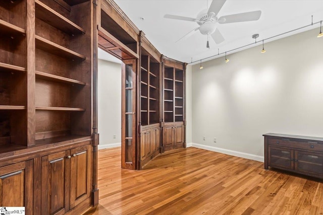 empty room featuring ceiling fan, rail lighting, built in features, and light wood-type flooring