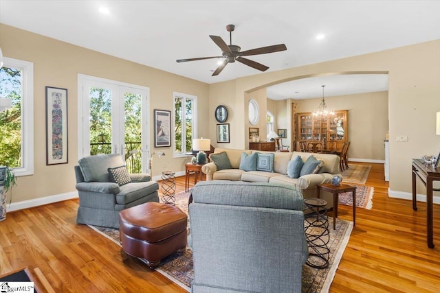 living room with ceiling fan with notable chandelier and light hardwood / wood-style flooring