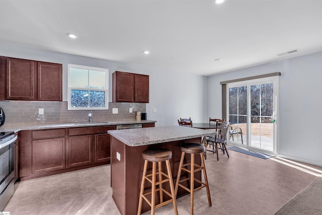 kitchen with appliances with stainless steel finishes, a center island, decorative backsplash, sink, and a breakfast bar area