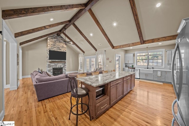 kitchen with a kitchen island, stainless steel appliances, a stone fireplace, light wood-type flooring, and ceiling fan