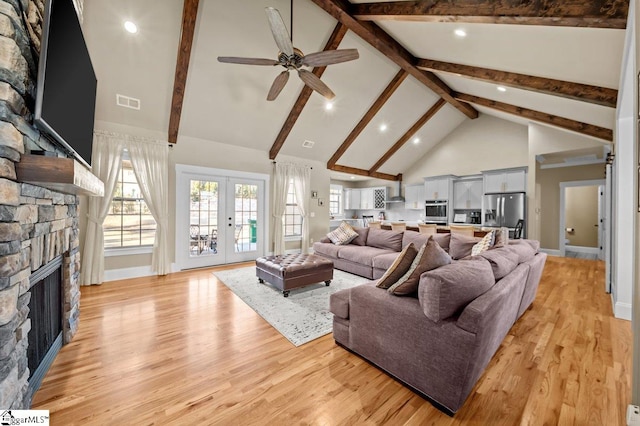 living room featuring french doors, beamed ceiling, a stone fireplace, light wood-type flooring, and high vaulted ceiling