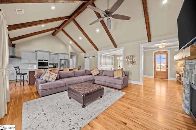 living room with light hardwood / wood-style floors, ceiling fan with notable chandelier, a stone fireplace, and high vaulted ceiling