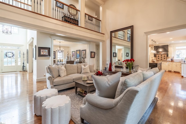 living room featuring a notable chandelier, light hardwood / wood-style floors, a towering ceiling, sink, and ornamental molding